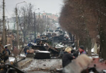 Russia Takes Aim at Urban Areas; Biden Vows Putin Will ‘Pay’ People look at the gutted remains of Russian military vehicles on a road in the town of Bucha, close to the capital Kyiv, Ukraine, Tuesday, March 1, 2022. Photo: Serhii Nuzhnenko / AP