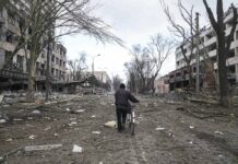 Russians Keep Pressure on Mariupol; Massive Convoy Breaks Up A man walks with a bicycle in a street damaged by shelling in Mariupol, Ukraine, Thursday, March 10, 2022. Photo: Evgeniy Maloletka / AP
