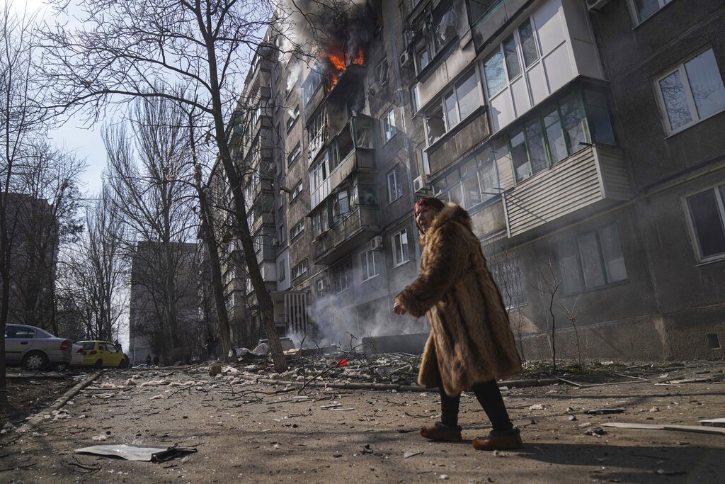A woman walks past a burning apartment building after shelling in Mariupol, Ukraine, Sunday, March 13, 2022. Photo: Evgeniy Maloletka / AP