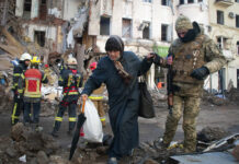 Russia’s Onslaught Continues Amid Optimism Over Talks A volunteer of the Ukrainian Territorial Defense Forces assists a woman to cross the street in Kharkiv, Ukraine, Wednesday, March 16, 2022. Photo: Andrew Marienko / AP