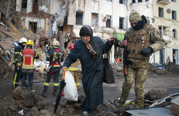 A volunteer of the Ukrainian Territorial Defense Forces assists a woman to cross the street in Kharkiv, Ukraine, Wednesday, March 16, 2022. Photo: Andrew Marienko / AP