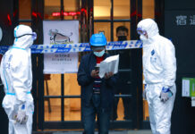 Much of Shanghai Locked Down as Mass COVID-19 Testing Begins FILE - A delivery man walks by police officers with protective suit outside of a hotel in Shanghai, China, on March 15, 2022. Photo: AP