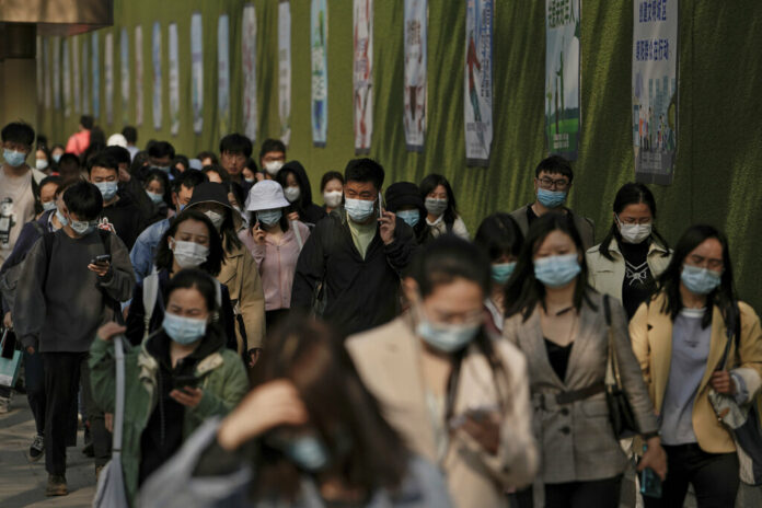 People wearing face masks to help protect from the coronavirus walk by a wall displaying propaganda posters as they head to work at the Central Business District during the morning rush hour, Monday, April 18, 2022, in Beijing. Photo: Andy Wong / AP