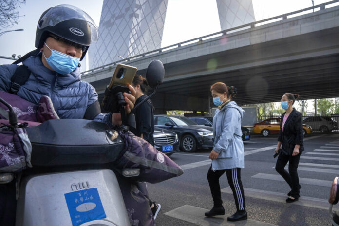 Commuters wearing face masks walk across an intersection in the central business district in Beijing, Tuesday, April 19, 2022. Photo: Mark Schiefelbein / AP