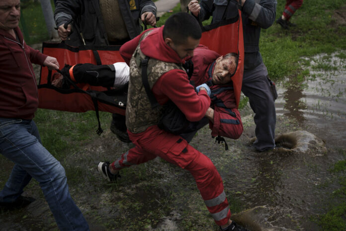 An emergency worker is helped by locals to carry a man to an ambulance following a Russian bombardment in Kharkiv, Ukraine, Wednesday, April 27, 2022. Photo: Felipe Dana / AP