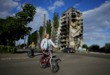 Ukraine: 200 Bodies Found in Basement in Mariupol’s Ruins A girl rides a bicycle in front of houses ruined by shelling in Borodyanka, Ukraine, Tuesday, May 24, 2022. Photo: Natacha Pisarenko / AP