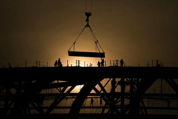 FILE - Workers are silhouetted against a sunset as they handle a steel frame on the roof of the Workers' Stadium under construction in Beijing, China, Monday, Feb. 28, 2022. Photo: Andy Wong / AP File