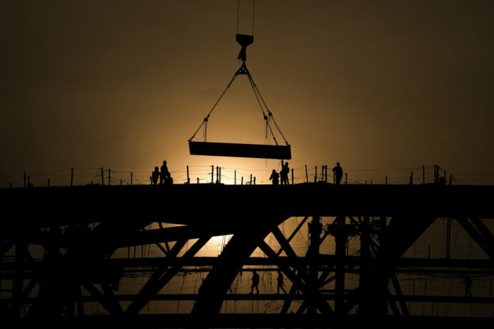 FILE - Workers are silhouetted against a sunset as they handle a steel frame on the roof of the Workers' Stadium under construction in Beijing, China, Monday, Feb. 28, 2022. Photo: Andy Wong / AP File FILE - Workers are silhouetted against a sunset as they handle a steel frame on the roof of the Workers' Stadium under construction in Beijing, China, Monday, Feb. 28, 2022. Photo: Andy Wong / AP File