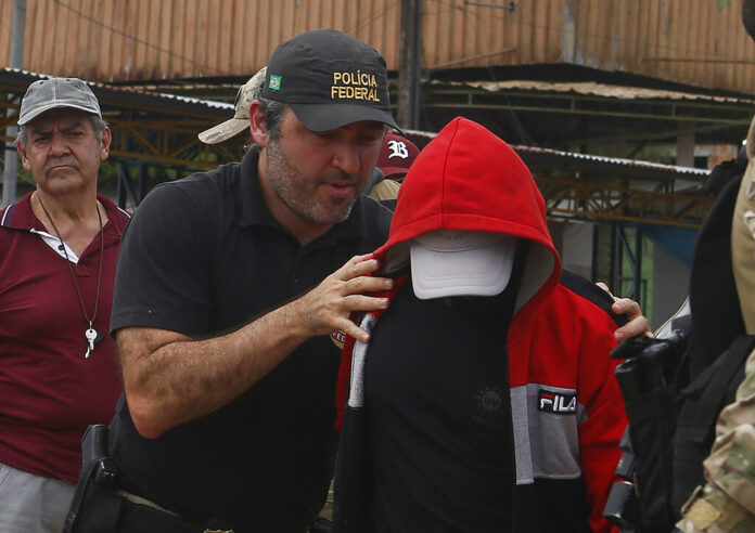 A federal police officer escorts a suspect towards a river in the area where Indigenous expert Bruno Pereira and freelance British journalist Dom Phillips disappeared, in Atalaia do Norte, Amazonas state, Brazil, Wednesday, June 15, 2022. Photo: Edmar Barros / AP