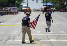 Parade Shooting Suspect Bought 5 Weapons Despite Threats A member of the FBI's evidence response team removes an American flag one day after a mass shooting in downtown Highland Park, Ill., Tuesday, July 5, 2022. Photo: Charles Rex Arbogast / AP