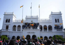 Sri Lanka Waits in Confusion, Anger for President To Resign Sri Lankan protesters, some carrying national flags, stand on top of prime minister Ranil Wickremesinghe 's office, demanding he resign after president Gotabaya Rajapaksa fled the country amid economic crisis in Colombo, Sri Lanka, Wednesday, July 13, 2022. Photo: Eranga Jayawardena / AP