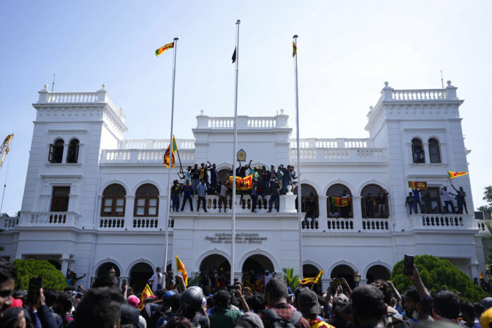 Sri Lankan protesters, some carrying national flags, stand on top of prime minister Ranil Wickremesinghe 's office, demanding he resign after president Gotabaya Rajapaksa fled the country amid economic crisis in Colombo, Sri Lanka, Wednesday, July 13, 2022. Photo: Eranga Jayawardena / AP Sri Lankan protesters, some carrying national flags, stand on top of prime minister Ranil Wickremesinghe 's office, demanding he resign after president Gotabaya Rajapaksa fled the country amid economic crisis in Colombo, Sri Lanka, Wednesday, July 13, 2022. Photo: Eranga Jayawardena / AP