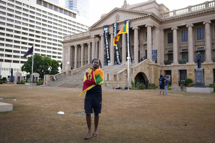 A protester walks wrapping a national flag around his shoulders in the compound of presidential secretariat in Colombo, Sri Lanka, Friday, July 15, 2022. Photo: Eranga Jayawardena / AP