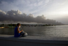 Raging Fire Consumes 4th Tank at Cuba Oil Storage Facility A resident sits on the malecon sea wall as smoke rises in the background from a deadly fire at a large oil storage facility in Matanzas, Cuba, Tuesday, Aug. 9, 2022. Photo: Ismael Francisco / AP