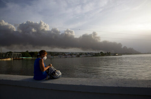 A resident sits on the malecon sea wall as smoke rises in the background from a deadly fire at a large oil storage facility in Matanzas, Cuba, Tuesday, Aug. 9, 2022. Photo: Ismael Francisco / AP