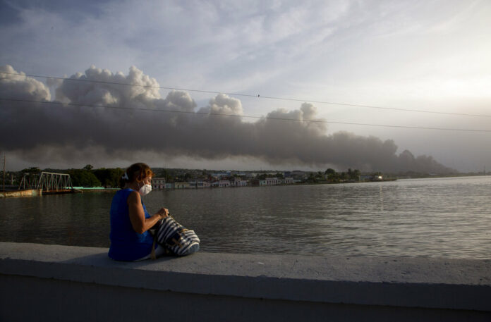 A resident sits on the malecon sea wall as smoke rises in the background from a deadly fire at a large oil storage facility in Matanzas, Cuba, Tuesday, Aug. 9, 2022. Photo: Ismael Francisco / AP