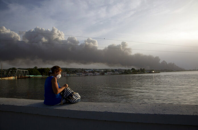 A resident sits on the malecon sea wall as smoke rises in the background from a deadly fire at a large oil storage facility in Matanzas, Cuba, Tuesday, Aug. 9, 2022. Photo: Ismael Francisco / AP A resident sits on the malecon sea wall as smoke rises in the background from a deadly fire at a large oil storage facility in Matanzas, Cuba, Tuesday, Aug. 9, 2022. Photo: Ismael Francisco / AP