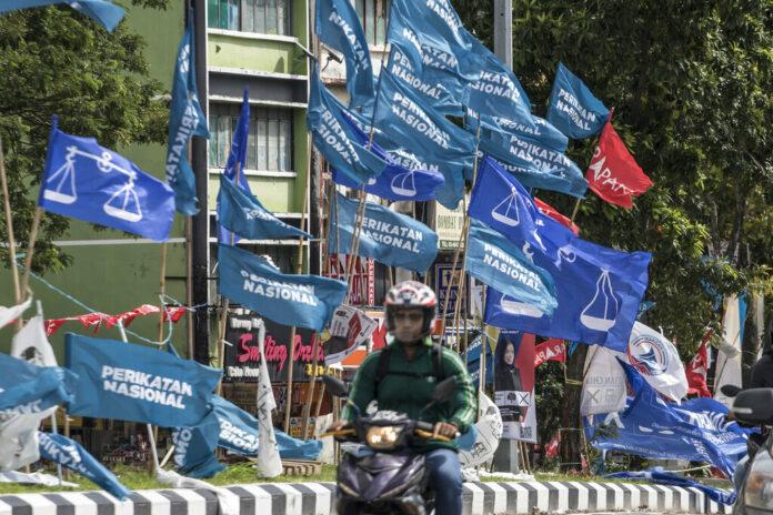 Motorcycles passing by campaign flags of Malaysia's ruling National Front coalition, or Barisan Nasional (blue) and Pakatan Harapan (Alliance of Hope) coalition (red) displayed in Kuala Lumpur, Malaysia, Sunday, Nov. 20, 2022. Photo: Ahmad Yusni / AP