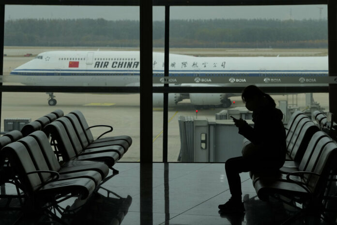 A passenger checks her phone as an Air China passenger jet taxi past at the Beijing Capital International airport in Beijing, Saturday, Oct. 29, 2022. Photo: Ng Han Guan / AP