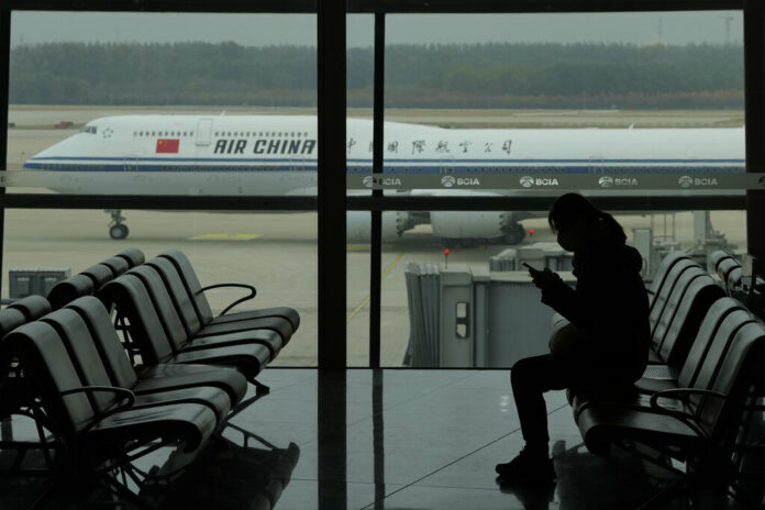 A passenger checks her phone as an Air China passenger jet taxi past at the Beijing Capital International airport in Beijing, Saturday, Oct. 29, 2022. Photo: Ng Han Guan / AP A passenger checks her phone as an Air China passenger jet taxi past at the Beijing Capital International airport in Beijing, Saturday, Oct. 29, 2022. Photo: Ng Han Guan / AP