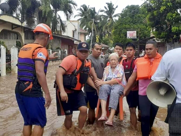In this image provided by the Philippine Coast Guard, an elderly woman sits on a chair while being carried by coast guard personnel wading through floodwaters in Plaridel, Misamis Occidental province in the southern Philippines, Monday, Dec. 26, 2022. Photo: Philippine Coast Guard via AP
