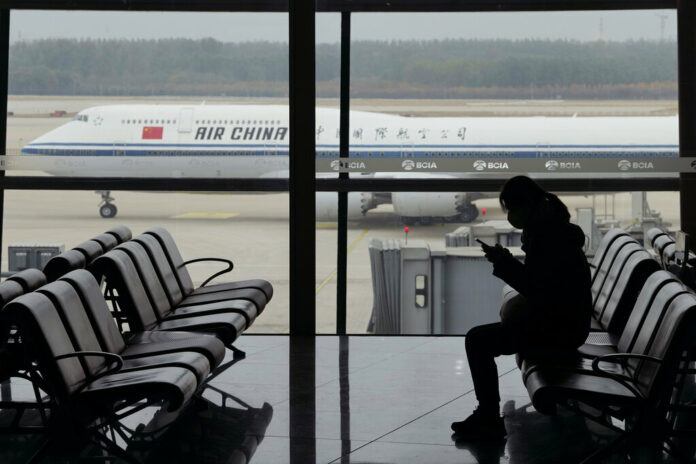 FILE - A passenger checks her phone as an Air China passenger jet taxi past at the Beijing Capital International airport in Beijing, Saturday, Oct. 29, 2022. Photo: Ng Han Guan / AP File FILE - A passenger checks her phone as an Air China passenger jet taxi past at the Beijing Capital International airport in Beijing, Saturday, Oct. 29, 2022. Photo: Ng Han Guan / AP File