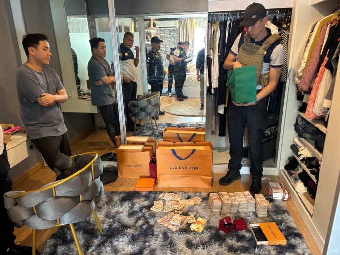 A police officer inspects cash and luxury items during a raid of a condominium unit in Bangkok belonging to one of the scammers on Nov. 14, 2023.