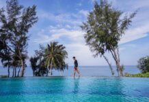 Why Thailand Beach Resorts Are the Ultimate Travel Destination A man walking along an infinity pool by the beach surrounded by palm trees at a Thailand beach resort.