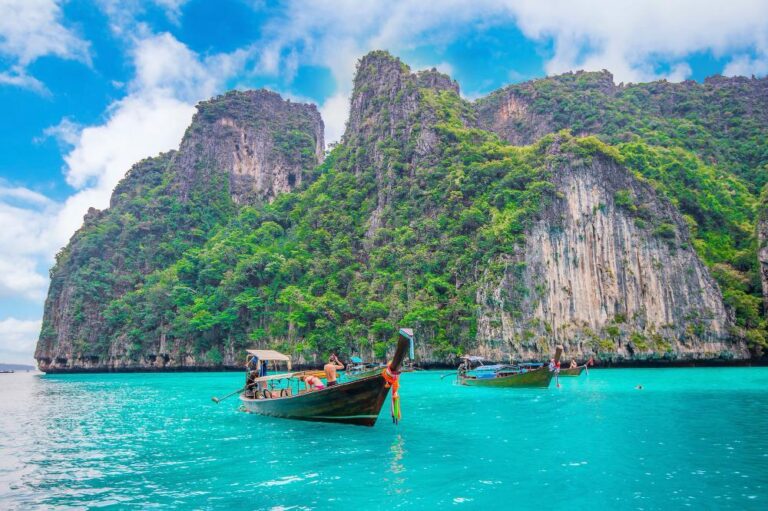 Traditional long-tail boats floating on crystal-clear turquoise water with limestone cliffs in Krabi, Thailand.