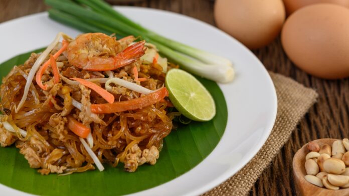 Padthai shrimp in a white dish with lime and eggs on wooden tabl