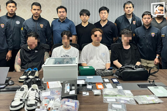 Thai officials stand behind the arrested South Korean men with seized evidence laid out on the table ahead of them.