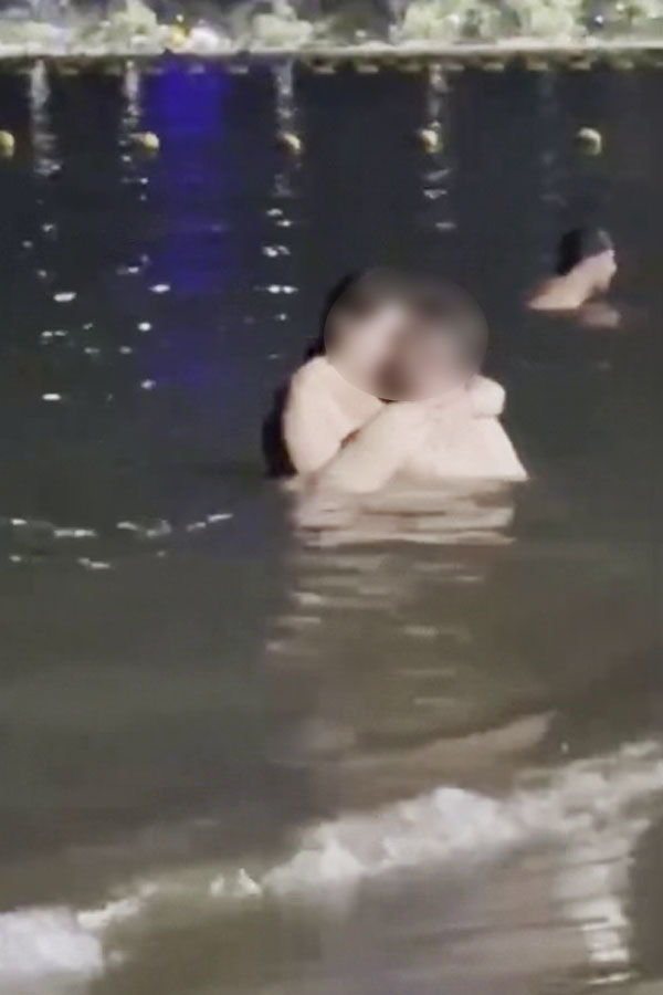 A couple is seen embracing romantically in the water near the beach shore, with their faces blurred out.