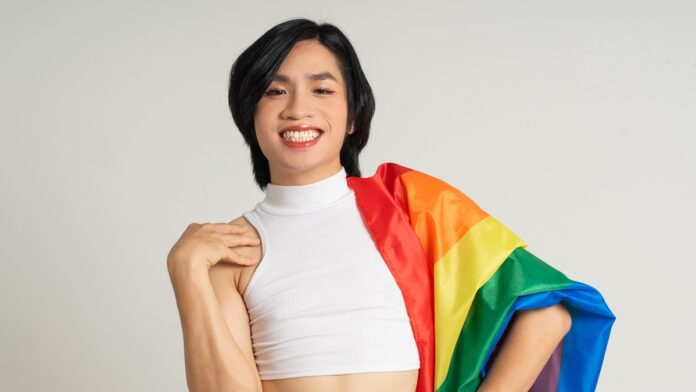 Image of Asian gay man holding a rainbow flag confidently posing