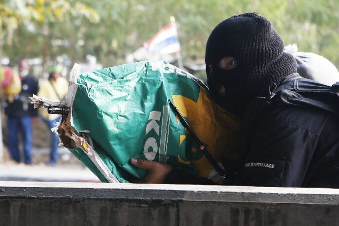 A masked gunman fires a rifle concealed in a bag from anti-government protesters' position, 1 February 2014