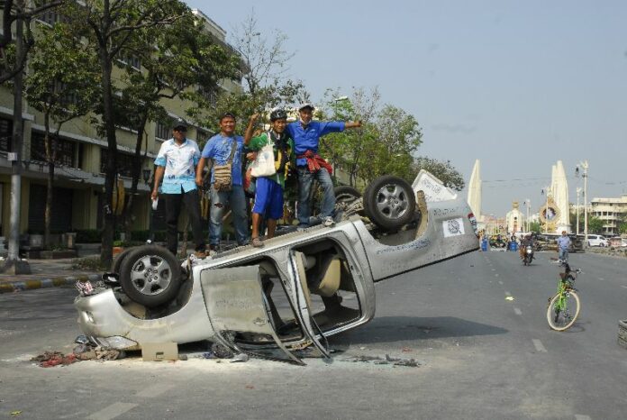 Anti-government protesters pose with a car damaged by previous clashes between police and protesters, 20 February 2014