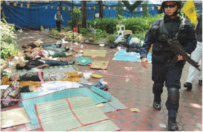 A member of the security force walk past dead bodies of 6 civilians killed in Wat Pathumwanararm Temple, 20 May 2010