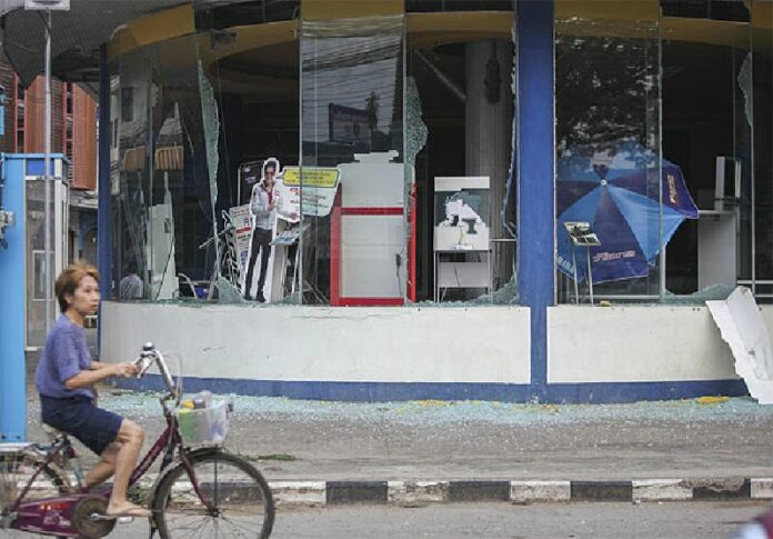 A woman cycles past a damaged building in Chiang Rai’s Phan district – Photo Pattarapong Chatpattarasill (Chiang Rai Times).