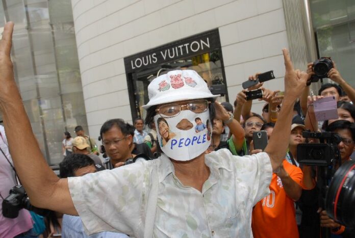 A 71-year-old woman was mobbed and escorted away by police for wearing a mask with an anti-coup message, 1 June 2014.