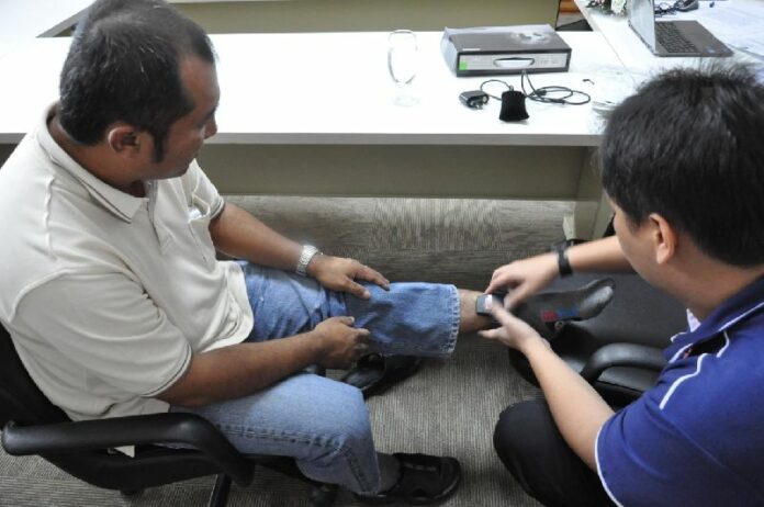 A police officer installs the monitoring device on Mr. Somwang's ankle.