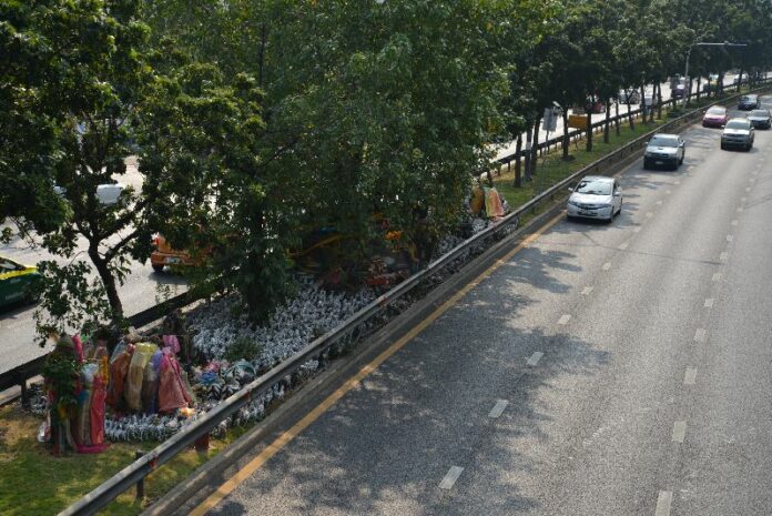 Many believers have crossed the road to plant offerings by a Bo tree in the center.