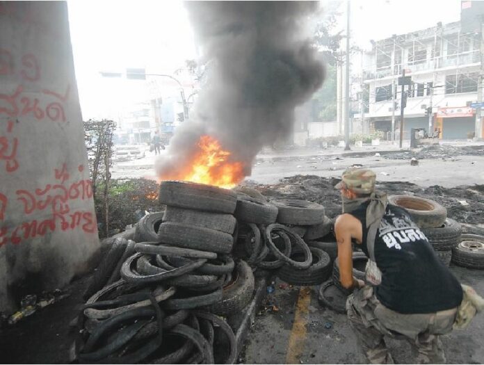 A Redshirt demonstrator hides behind a pile of burning tires while he watches the movement of soldiers in Din Daeng district, 18 May 2010