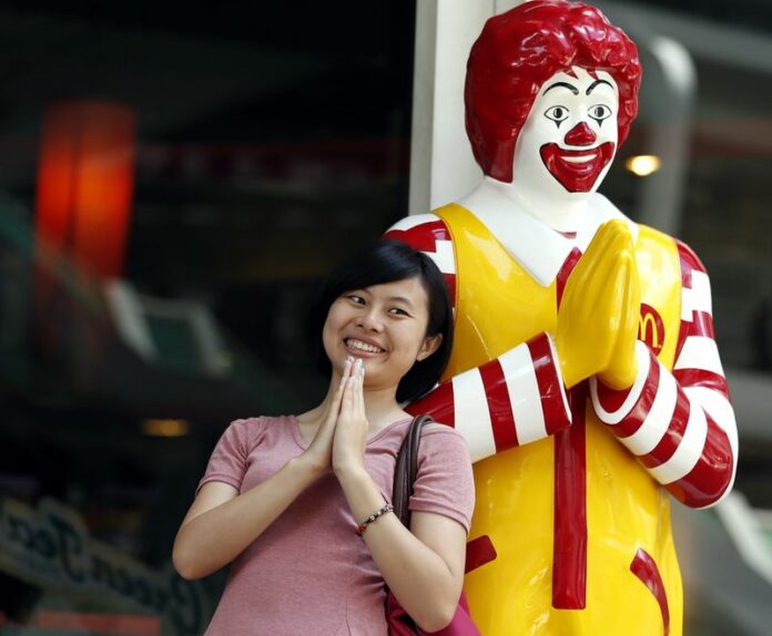A Chinese tourist makes a traditional Thai greeting gesture beside a Ronald McDonald statue in central Bangkok, Thailand, 30 April 2013. Thousands of Chinese tourists visiting Thailand during their New Year holiday will receive "tourism manuals" in an effort to curb offensive behaviour, officials said Monday. EPA/RUNGROJ YONGRIT<br />