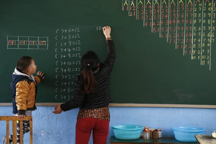 A Chinese kindergarten teacher writes math equations on a board as a young boy looks on at the Qiang Jian Wen Wu school in the west side of Beijing. EPA/ROLEX DELA PENA<br />