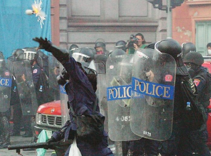 A police officer hurls a tear gas grenade toward the protesters in front of the Parliament in Bangkok, 7 October 2008