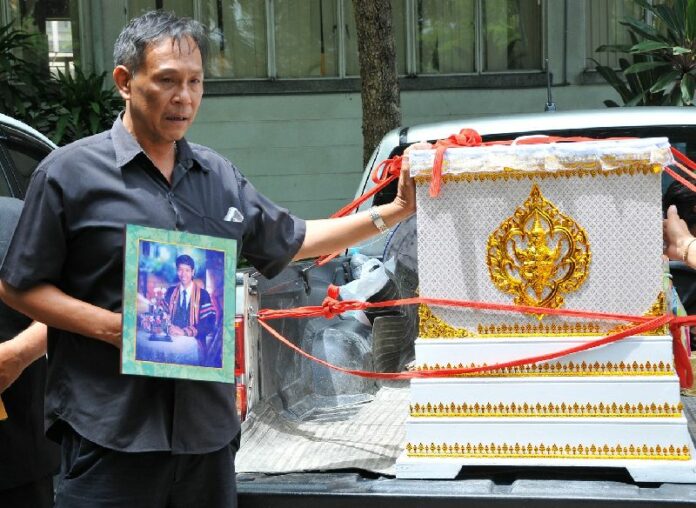 Assaneechaiyapol Charoenwinit's father holding a portrait of his son beside his coffin, 8 June 2015.<br />