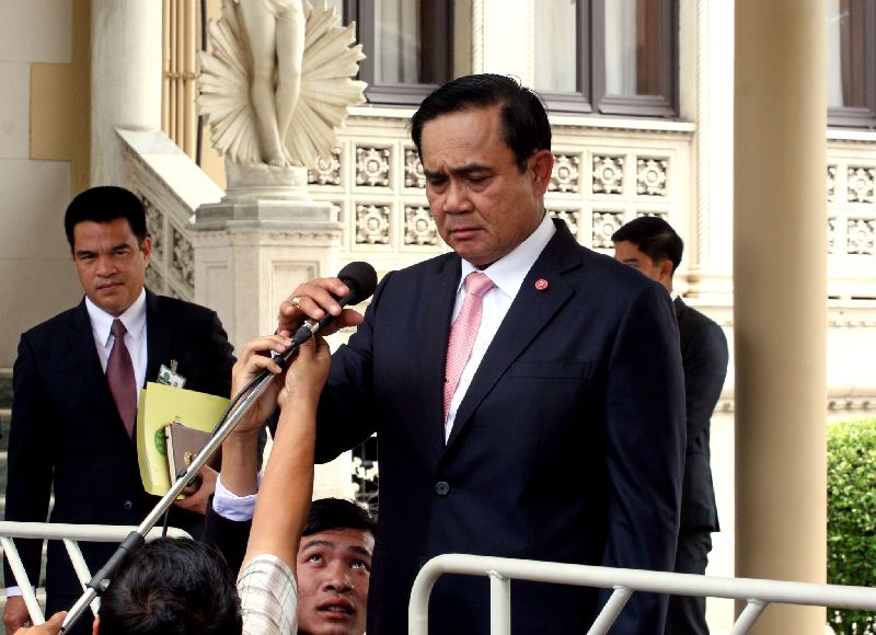 A journalist helps adjust Gen. Prayuth Chan-ocha's microphone during a press conference at the Government House, 25 June 2015.