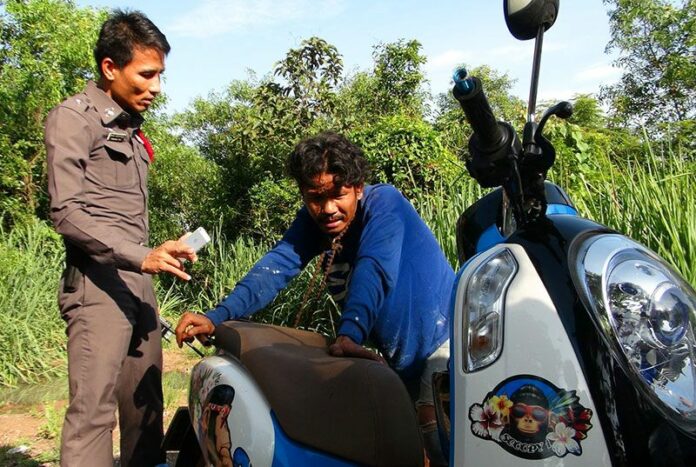 Tethered by the neck to his own motorcycle with its drive chain, Pichai Angpasi tells his story to a police officer this morning while waiting for help.
