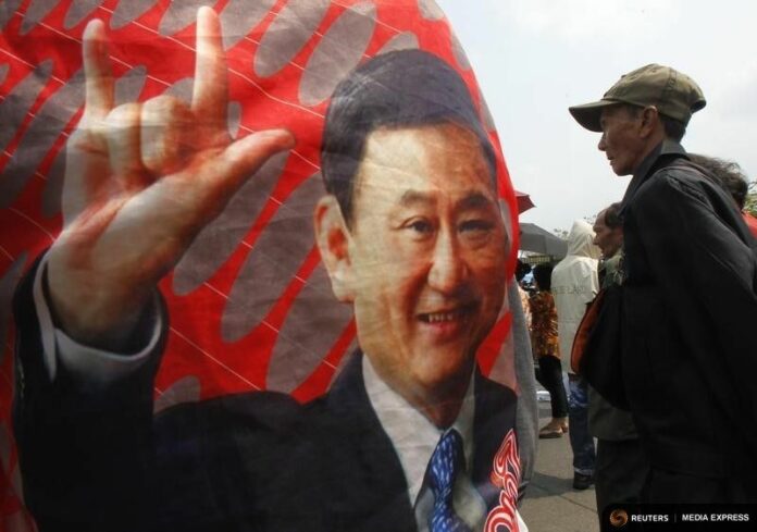 A government supporter stands next to a picture of former Thai Prime Minister Thaksin Shinawatra during a rally outside the National Anti-Corruption Commission office in Nonthaburi province, on the outskirts of Bangkok on 27 Feb., 2014. Photo: Reuters / Chaiwat Subprasom
