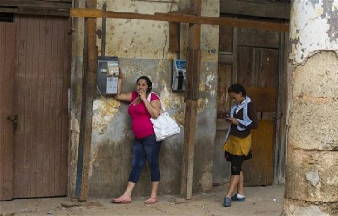 A woman speaks on a public phone as a student looks at her mobile phone in Havana, Cuba, Jan. 26, 2016. Photo: Desmond Boylan / AP