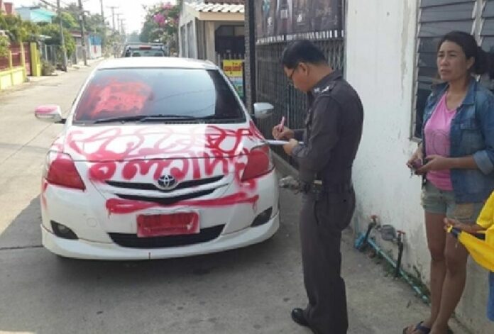 A police officer inspects the car of Thitirat Lheesuwan, 43, on Saturday after it was mysteriously painted with offensive language in Ratchaburi province.